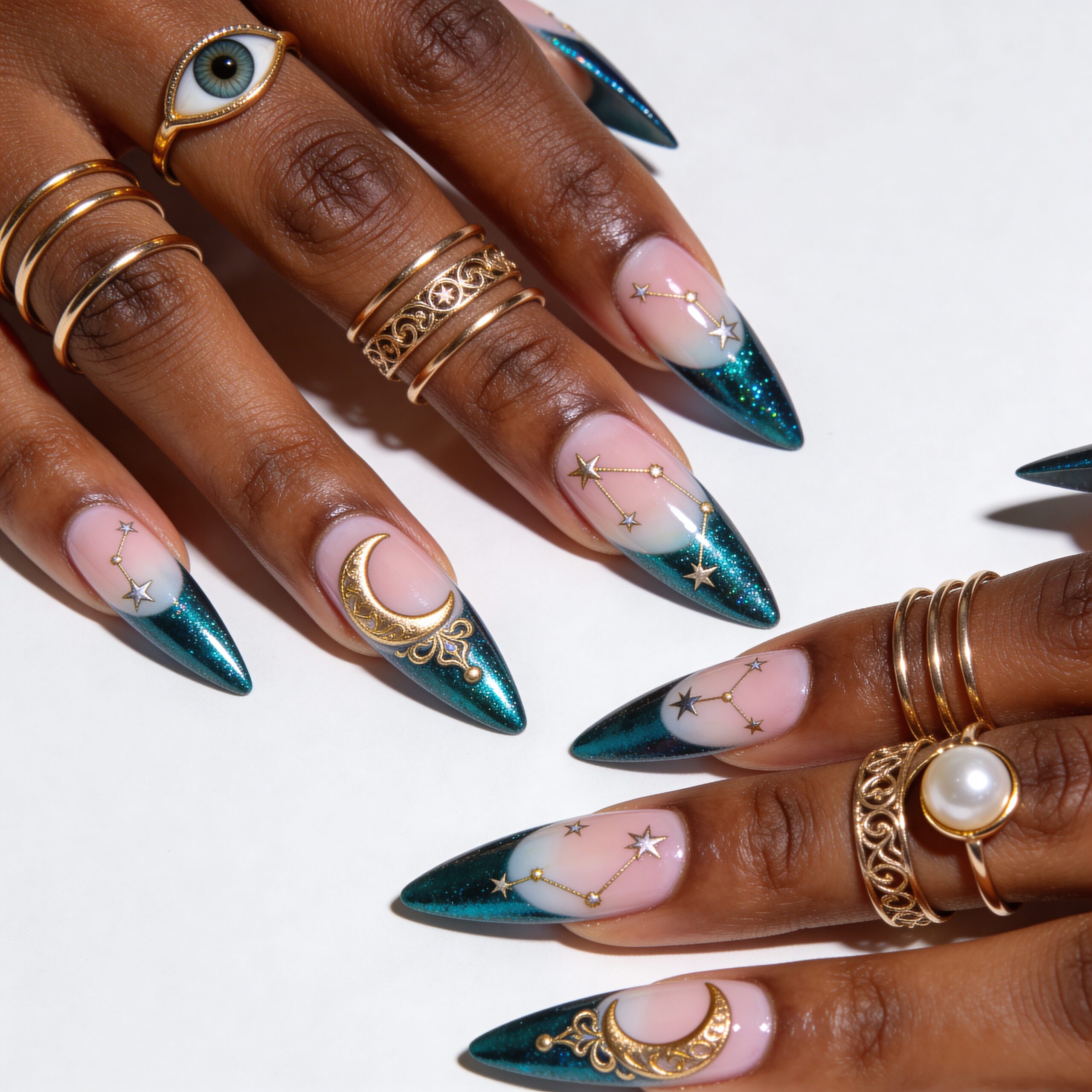 Luxurious celestial blue and gold nail art on elegant hands featuring teal chrome glitter, soft pink bases with intricate gold crescent moons, stars, and ornate filigree details, accented with gold stacking rings